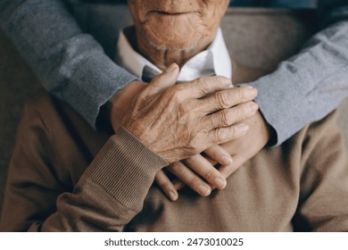Happy healthcare worker hugging a senior man at home and support encouraging old people. A happy patient is holding the caregiver for a hand while spending time together. Elderly health care concept.