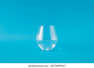 简洁干净的图像，以鲜艳的蓝色背景为背景，展示半杯水。简约的设计凸显了水和玻璃的清澈，营造出清新的感觉
