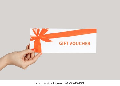 Closeup of woman hand showing paper card, gift voucher, present for free shopping. Indoor studio shot isolated on gray background.