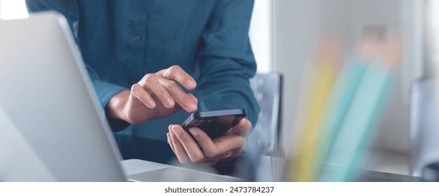Biznesmenka korzystająca ze smartfona, pracująca na laptopie w biurze, zbliżenie. Azjatka korzystająca ze smartfona, szukająca informacji, surfująca po internecie z laptopem na biurowym stole