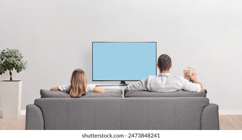 Rear view shot of a father and child holding popcorn sitting on a sofa and watching tv