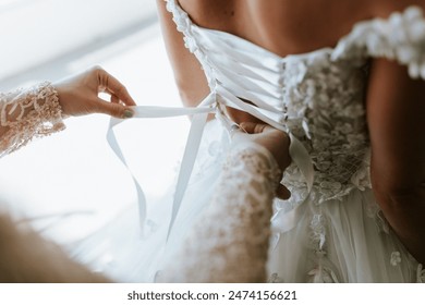 A bride or bridesmaid carefully adjusts the laces or buttons of a wedding dress, highlighting the detailed preparations and anticipation before the ceremony.