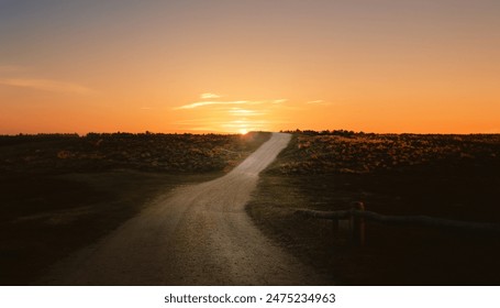 Een onverharde weg die naar de zonsondergang leidt met een gouden lucht, omgeven door gras en velden.