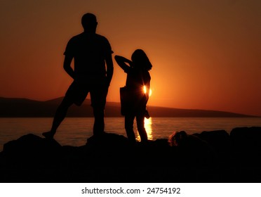 Silhouetten van man en meisje die op rotsen staan ​​en naar de zonsondergang kijken