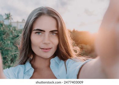 Amber Golden Hour Krupni plan žene okupane u zlatnočasovnom svjetlu koja pravi selfi na zalasku sunca u ljetnom parku. Sretni turist uživa u snimanju selfija na otvorenom za uspomene