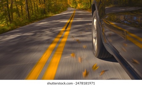 GROS PLAN Une voiture SUV noire circulant sur une double route forestière jaune, le long d'arbres colorés, un jour d'automne. Détail d'un pneu de voiture qui tourne pendant la conduite à travers une forêt d'automne lumineuse sous le soleil d'automne. Roulement d'un pneu de voiture