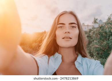 Amber Golden Hour Nga afër një grua e larë në dritën e orës së artë duke bërë selfie në perëndimin e diellit në parkun veror. Turisti i lumtur kënaqet duke bërë foto selfie jashtë për kujtime