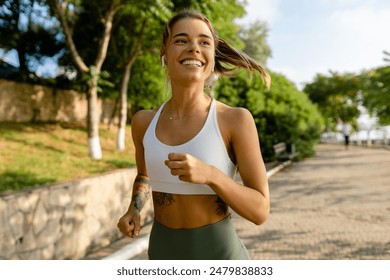 jolie jeune femme blonde souriante faisant des exercices de sport en courant, en faisant du jogging dans le parc le matin, coupe skinny en tenue de sport, leggings et haut, motivation pour la santé en été, corps fort, chaud