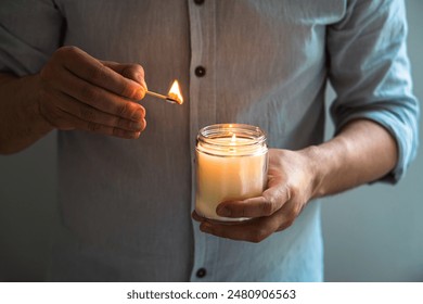 Man holding a burning candle in his hands, elegant young man with candle jar, meditation and mindfulness concept