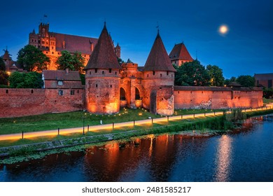 Castle of theTeutonic Order in Malbork by the Nogat river at night with full moon.