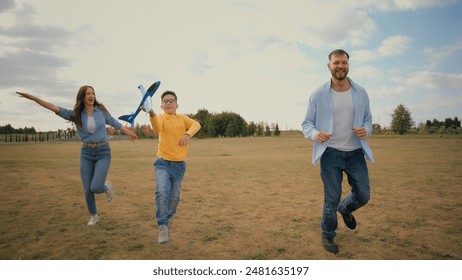 Linda familia caucásica vacaciones de fin de semana hombre feliz padre papá correr mujer madre mamá corriendo jugar niño pequeño niño hijo jugando juguete juego avión picnic estilo de vida activo naturaleza prado parque