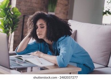 صورة لامرأة جميلة متعبة ترتدي قميصًا أنيقًا وتجلس على الأريكة وتدرس من المنزل وتستخدم جهاز ماك بوك في غرفة داخلية