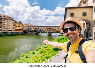 Young man taking selfie in front of Ponte Vecchio bridge in Florence Tuscany Italy, during her summer vacations in Europe.