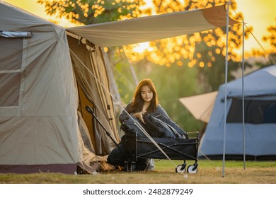 Usmívající se sebevědomá mladá žena sólo trekking kemp balení různých kempinkových vybavení na kempingový vozík do stanu v kempu pod dramatickou večerní oblohou. Oranžový západ slunce a hory v pozadí