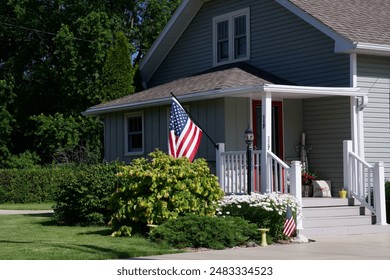 a house with a white porch and railings, and an american flag flying in the front of the two story building on a sunny july day