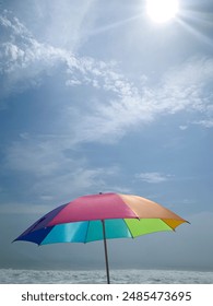 Sonne scheint auf den Regenbogenschirm in der Nähe des Meeres