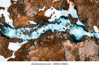 Pamje ajrore e një lumi të gjallë që pret borën dhe terrenin shkëmbor, Islandë.