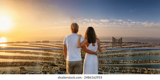 A romantic couple on a city vacation trip enjoys the panoramic sunset view of the Palm island at Dubai, UAE