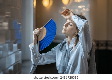 Una mujer, cansada del mal tiempo en el trabajo, sufriendo de calor o de dolor de cabeza, del aire sofocante y cargado en una oficina sin aire acondicionado, salió al pasillo, abanicándose con un abanico de papel.