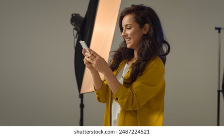 Happy carefree Caucasian woman girl female blogger influencer smiling turn on music mobile phone device speakers dancing singing. Model vlogger streamer having fun enjoying song moving alone in studio