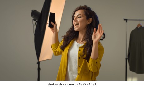 Happy carefree Caucasian woman girl female blogger influencer smiling turn on music mobile phone device speakers dancing singing. Model vlogger streamer having fun enjoying song moving alone in studio