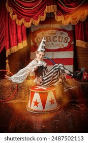 Ënnerhaalung. E jonken Zirkusartist an engem Harlequinkostüm spillt op der Bühn vun engem ale Zirkus. Vintage Zirkus Kuliss.