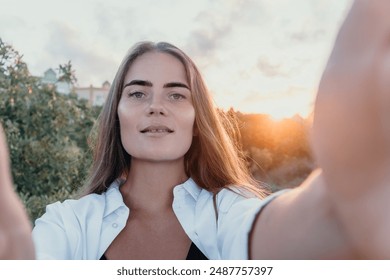 Amber Golden Hour Nga afër një grua e larë në dritën e orës së artë duke bërë selfie në perëndimin e diellit në parkun veror. Turisti i lumtur kënaqet duke bërë foto selfie jashtë për kujtime