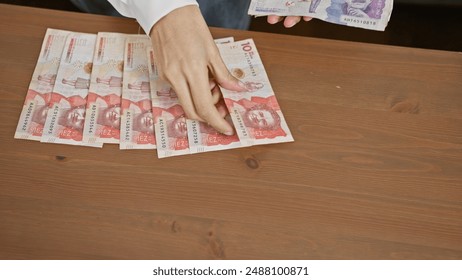 Młoda kobieta liczy kolumbijskie peso na drewnianym stole w domu, co ilustruje finanse i budżetowanie w warunkach domowych.
