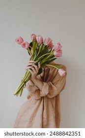 Conceito de moda estética. Buquê de tulipas rosa nas mãos de uma mulher. Mulher vestida de bege e branco. Tons e cores neutros e suaves em tons pastel. Estilo minimalista.