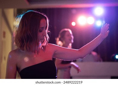 Young girl in the foreground dancing and enjoying music in the nightclub with a nice pink light effect