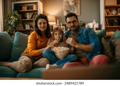 Keluarga, ibu ayah dan anak perempuan memegang panci popcorn dan tertawa sambil menonton TV