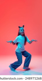 Full-length image of smiling young girl in casual clothes, white t-shirt and jeans, dancing modern dance style against pink background in neon light. Concept of childhood, human emotions, fashion