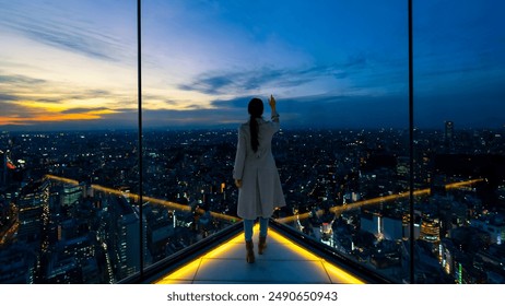 Happy Asian woman looking beautiful metropolis cityscape at skyscraper building rooftop at sunset. Attractive girl relax and enjoy outdoor lifestyle travel and shopping in the city on holiday vacation