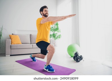 Photo of handsome good mood guy wear yellow t-shirt enjoy squatting doing morning sport exercises indoors room home house