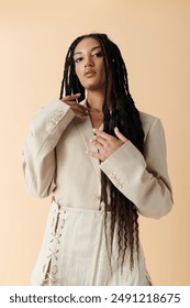 A stylish African American woman poses in a white blazer and skirt against a neutral beige background.