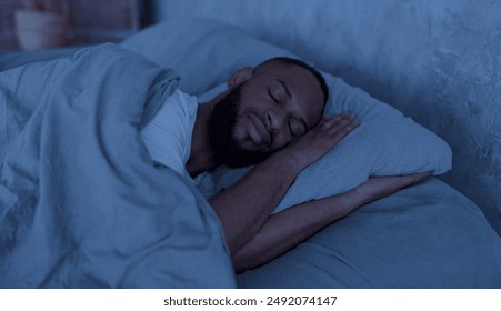 Healthy Sleeping Concept. Portrait of happy young well-slept African American man lying in bed with closed eyes, resting in bedroom on the side in the dark night, having hap