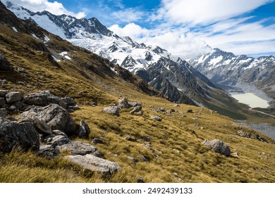 Uma paisagem montanhosa acidentada na Nova Zelândia, com picos cobertos de neve, geleiras e um vale verdejante.