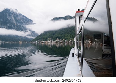 Vista riflessa dal finestrino del traghetto del famoso e pittoresco villaggio di Hallstatt e delle montagne nuvolose, Gmunden, Austria