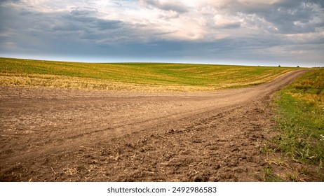 Zonnige dag op een onverharde weg door een schilderachtig landschap met groene velden onder een bewolkte lucht