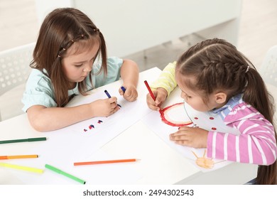 أطفال صغار لطيفون يرسمون على الطاولة في الداخل