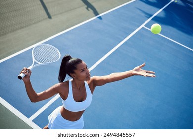 Black woman, racket and playing tennis in outdoor, confident serve and sports workout on court. Female person, fitness and ball for game or match at club, exercise and energy for training practice