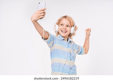 Caucasiano feliz jovem pré-adolescente menino criança do sexo masculino criança primária escola média aluno adolescente tirando selfie no telefone enquanto ouve música em fones de ouvido isolados no fundo branco