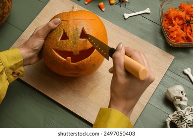 Mulher esculpindo abóbora de Halloween em mesa de madeira verde