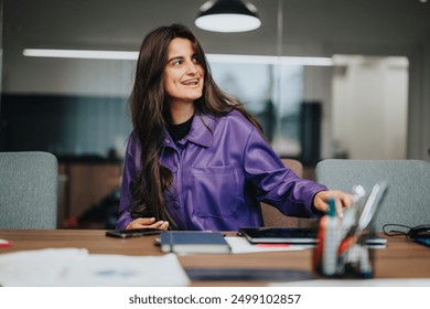 Una giovane donna concentrata che indossa una giacca viola brillante si gode il suo lavoro in un ambiente d'ufficio vivace, dimostrando produttività ed energia positiva sul posto di lavoro.