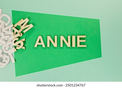 Populär a modern Puppelchen Meedchen Moudenumm ANNIE an hëlzent engleschsproocheg Kapitalbuschtawen aus engem Koup Bréiwer op engem gréngen Hannergrond agerummt
