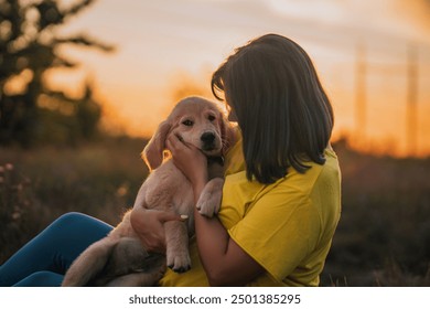 愛くるしいゴールデンレトリバーの子犬と飼い主の女性。田園風景を背景に、楽しい時間を過ごす幸せそうな犬。可愛らしい犬。狩猟犬種。高画質写真