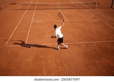 Top view image of young man, tennis player in motion on clay court, playing tennis, practicing forehand hit. Dynamics and focus. Concept of sport, competition, active and healthy lifestyle
