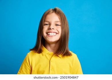 Happiness, joy and carefree. Portrait of young 9 years old girl in yellow polo shirt posing with big smile against blue studio background. Concept of childhood, kids emotions, lifestyle