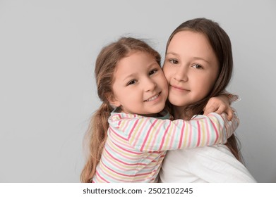 น้องสาวตัวน้อยน่ารักกอดกันบนพื้นหลังสีอ่อน ภาพระยะใกล้