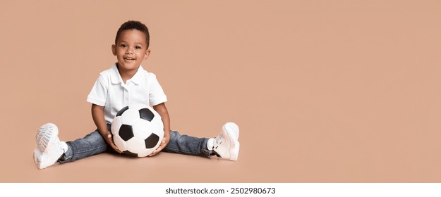 Kelas bola sepak untuk kanak-kanak. Potret budak hitam comel dengan bola sepak duduk di atas latar belakang studio kuning, ruang kosong